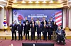 Officials pose beneath a Korea-U.S. banner in a formal hall, with a wheelchair user seated at right.