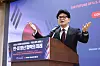 Speaker gesturing at a podium before a presentation screen with Korean and English text