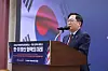 A suited speaker addresses an audience from a podium beside Korean event signage.