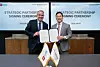 Two officials hold a signed document beside national flags at a partnership signing ceremony.