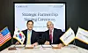Two executives sit at a signing table beside U.S. and South Korean flags.