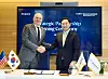 Two officials shake hands in front of a strategic partnership ceremony screen, with flags on a table.