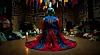 Person in a blue-and-red shaman costume kneeling in a dim, cluttered room