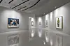 Modern white gallery displaying colorful framed artworks with reflections on a polished floor.
