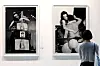 A visitor examines two framed black-and-white artworks on a white gallery wall.