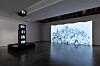 Contemporary gallery with a large projected artwork and a vertical illuminated display.