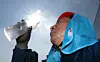 Construction worker in sun protection drinks from a plastic bottle under bright sunlight.