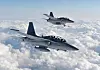 Two fighter jets fly over dense white clouds under a blue sky.