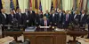 Officials gather behind a desk during a signing ceremony, with U.S. and international flags behind them.
