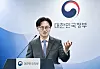 South Korean government official speaking at a podium beneath the national government emblem.