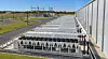 Rows of air-cooled chiller units sit beside a large industrial building and electrical substation.