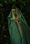 NANA as Hui-yeon stands in a dark forest beneath a translucent green cloak.