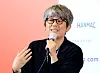 Kim Jong-kwan, wearing glasses, speaks into a microphone against a festival backdrop.