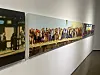 Gallery wall featuring a long panoramic painting of a large crowd and a partial adjacent artwork.