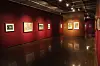 Empty art gallery with framed works on red walls and reflections on a polished floor.