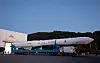 The Nuri rocket rests horizontally on a transporter outside a launch facility beneath a wooded hillside.