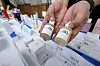 Hands hold two small bottles above boxed cosmetics and health supplements.