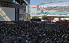 Large crowd seated outside Busan Cinema Center beneath a screen promoting a film festival open talk.
