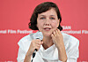 Maggie Gyllenhaal holds a microphone against a red film festival backdrop.