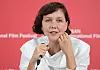 Maggie Gyllenhaal holds a microphone against a red film festival backdrop.