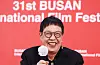 Ann Hui smiles while holding a microphone against a red Busan film festival backdrop.