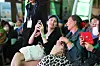 Seated audience members smile and hold smartphones at a crowded indoor event.