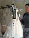 A blurred passerby walks beside a storefront displaying white wedding dresses in Seoul.