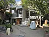 White abstract sculpture in a tree-lined courtyard outside a modern building.