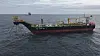 A colorful commercial workboat sails across dark, choppy sea beneath an overcast sky.