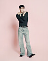 Fashion model posing in a dark top and light jeans against a pink backdrop.