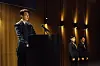 Kim Young-kwang stands at a podium in a warmly lit venue, with two men in the background.