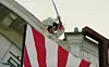 Worker in protective gear above a large American flag near a white historic building