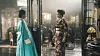 Two women in turquoise and patterned clothing face each other in a bright industrial-style interior.