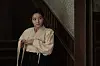 Woman in a cream blouse standing beside a wooden staircase indoors.