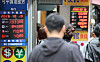 Exchange rates and currency symbols are shown outside a Myeongdong exchange shop as pedestrians walk past.