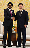 Lee Jae-myung and Ajay Banga shake hands in front of an ornate gold wall.