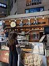 Customer viewing trays of savory pancakes at a brightly lit jeon stall in Seoul’s Mangwon Market.