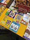 Several mobile payment QR codes are displayed on a bright yellow board beside fried food at a Seoul market stall.