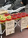 Red bowls of green and red grapes beside handwritten Korean price signs at a Seoul market stall.