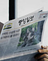 Hand holding a JoongAng Ilbo newspaper with headlines and a news photo.