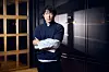 Song In-hyeok stands indoors with folded arms, wearing a dark sweater and holding a white garment.