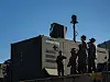 Military personnel gathered beside a large dark communications container outdoors.