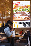 McDonald’s Big Arch burger poster displayed inside a Seoul restaurant beside seated diners.