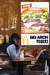 McDonald’s Big Arch burger poster displayed inside a Seoul restaurant beside seated diners.