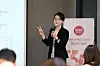 Presenter holding a microphone beside a Hetbahn anniversary sign at an indoor event.