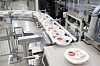 Round sealed containers move along a conveyor in an industrial food packaging facility.