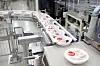Round sealed containers move along a conveyor in an industrial food packaging facility.