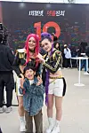 Two costumed performers pose with a smiling child at an indoor festival.