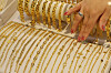 A hand arranges rows of gold chains in a jewelry display case.