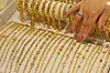 A hand arranges rows of gold chains in a jewelry display case.